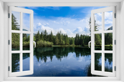 Fototapeta Naklejka Na Ścianę Okno 3D - Beautiful panoramic landscape with vibrant, green forest reflecting in the cold, crystal clear waters of an alpine lake on a sunny summer day