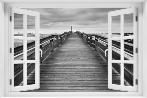 Fototapeta Naklejka Na Ścianę Okno 3D - Black And White Of A Wood Bridge That Leads To The Horizon By The Horizon Above Large Green Tall Grass Field Under The Stormy Sky And Rolling Clouds In Long Beach Washington