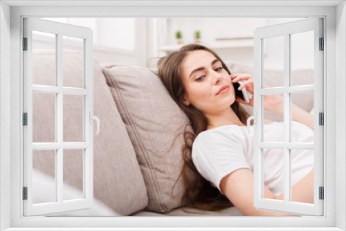 Young girl talking on mobile lying on beige couch