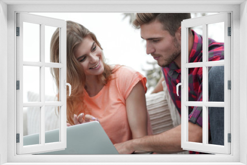 young couple is using a laptop and smiling while sitting on sofa at home