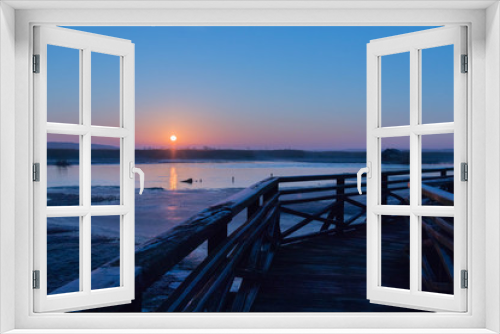 Fototapeta Naklejka Na Ścianę Okno 3D - the sun rises red over marshlands and swamps and a wooden bridge with a railing and birds resting on the water and among the reeds