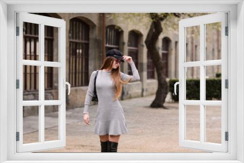 A beautiful girl in a cap is walking around the college. A student is enjoying a spring day. She is wearing sunglasses and a backpack.