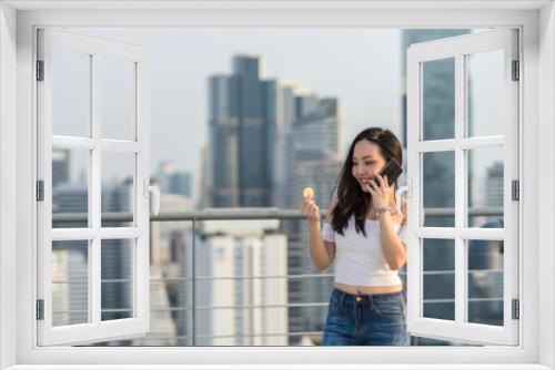 Working woman in casual suit holding bitcoin and using the smart mobile phone over the cityscape blurred background, business and cryptocurrency concept