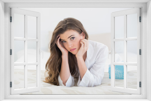 Depressed casual brown haired woman in white pajamas lying on her bed