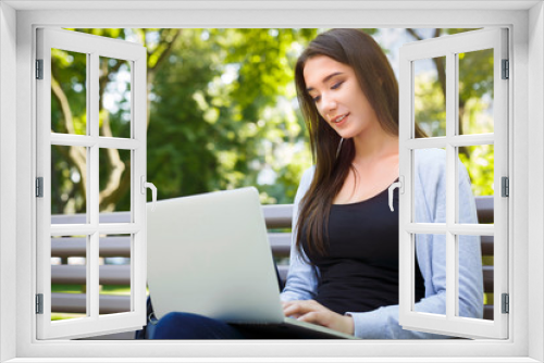 Motivated freelancer in the park. Girl on a bench, smiling and working with laptop