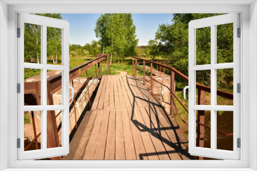 Fototapeta Naklejka Na Ścianę Okno 3D - landscape wooden bridge over the river, rusty metal railings, background green trees, blue sky