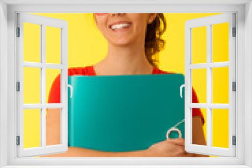 Beautiful young student woman holds folder over yellow background