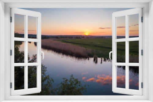Fototapeta Naklejka Na Ścianę Okno 3D - The calm surface of the river and the reflections of clouds, orange sunset, green fields and meadows in a quiet warm summer evening