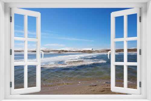 Fototapeta Naklejka Na Ścianę Okno 3D - Beaurtiful sunny day along the lake shore on spring day with ice and snow in water, blue sky in the background, sandy beach in foreground