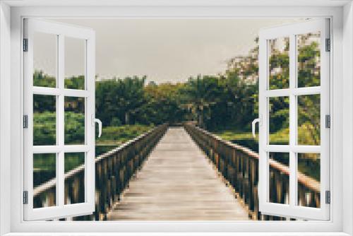 Fototapeta Naklejka Na Ścianę Okno 3D - Vertical shot of a misty wooden bridge stretching into the vanishing point with muskeg pond on the sides and the jungle forest in the distance, overcast summer day, Praia do Forte, state Bahia, Brasil