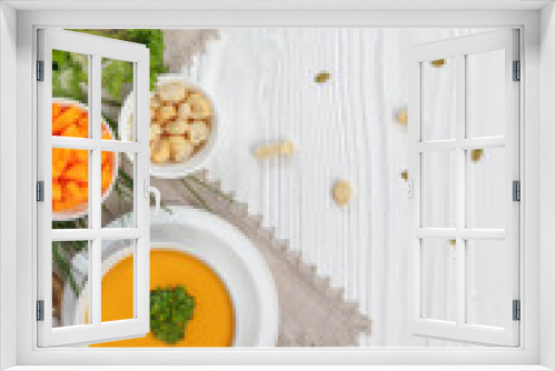 Fototapeta Naklejka Na Ścianę Okno 3D - Pumpkin cream soup with croutons, raw fresh pumpkin pieces and herbs on a white rustic wooden background, Autumn concept. 