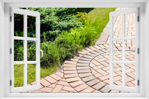 Fototapeta Naklejka Na Ścianę Okno 3D - Shrubs green in the garden . Shrubs near footpath. The stone pavement of the blocks. The paving is laid evenly. The road is good for ages. Gray and red stones.