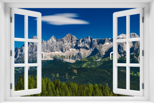 Fototapeta Naklejka Na Ścianę Okno 3D - Hohe Dachstein mountain range in Austria with green trees in the foreground and a white cloud on blue sky