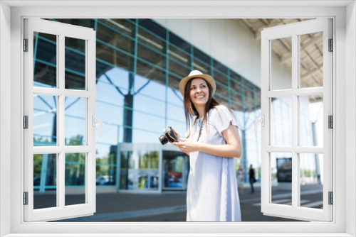 Young joyful traveler tourist woman holding retro vintage photo camera, looking aside at international airport. Female passenger traveling abroad to travel on weekends getaway. Air flight concept.