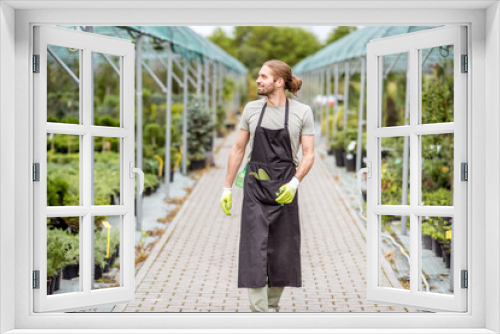 Handsome worker in uniform walking at the greenhouse with green plants for sale