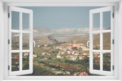 An elevated view over a Tenerife village of brightly coloured houses, the surrounding landscape and hills, the coast and ocean, all covered with the haze of La Calima (coastline of Costa Adeje)