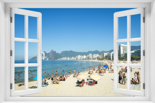 Fototapeta Naklejka Na Ścianę Okno 3D - Rio residents, known as cariocas, relax at the Arpoador section of Ipanema Beach with the city skyline and Two Brothers Mountain in the background.
