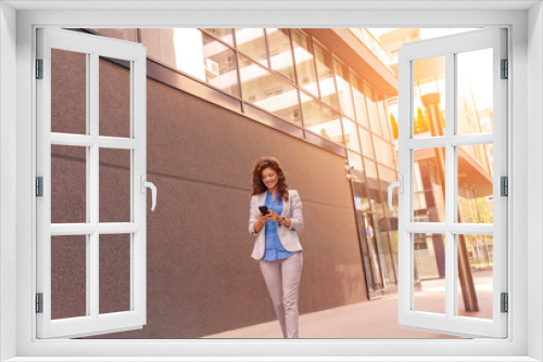 Businesswoman looking at her mobile phone while walking on street to office.