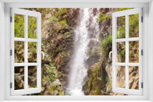 Fototapeta Naklejka Na Ścianę Okno 3D - Vertical view to a high waterfall in the mountains of the Altai with sprinkled drops of water through stones and rocks among green trees in the forest in sunny summer autumn weather with shining sun
