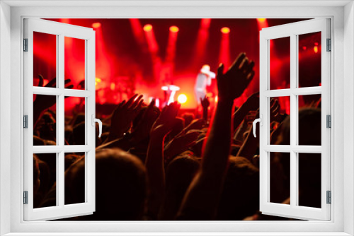 concert crowd during festival, hands of many people cheering musicians playing music on stage, red back light