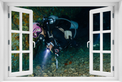 Fototapeta Naklejka Na Ścianę Okno 3D - A female SCUBA diver exiting an underwater cave on a tropical coral reef