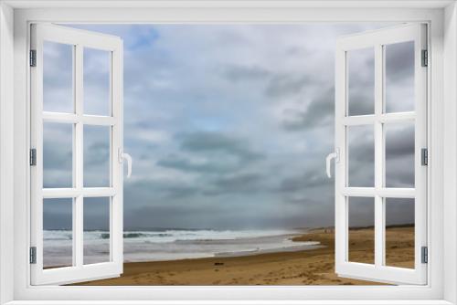 Fototapeta Naklejka Na Ścianę Okno 3D - Winter beach with a storm brewing out to sea - two people walk in distance with a dog and the waves crash and foam - RedHead beach NSW Australia