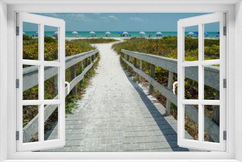 Fototapeta Naklejka Na Ścianę Okno 3D - Dramatic View of Wood Bridge looking toward a sandy Sanibel Beach on Sanibel Island with colorful umbrellas on a sunny day before Hurricane Ian