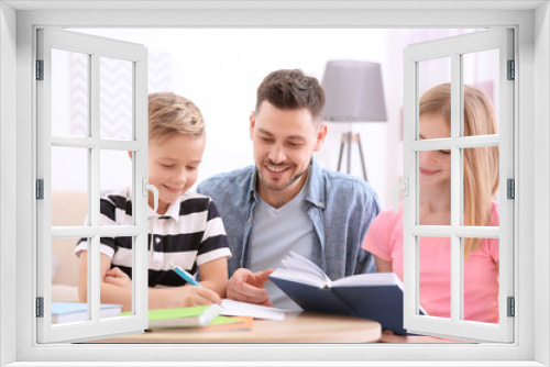 Cute little boy doing homework with father and sister