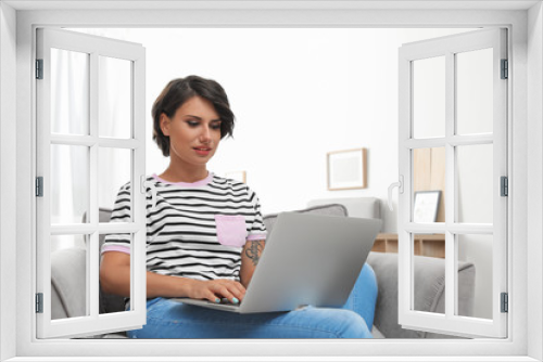 Young woman with modern laptop sitting in armchair at home