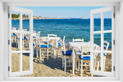 Fototapeta Naklejka Na Ścianę Okno 3D - A table with chairs of a greek tavern near the sea in a beach of Kos island, Greece.