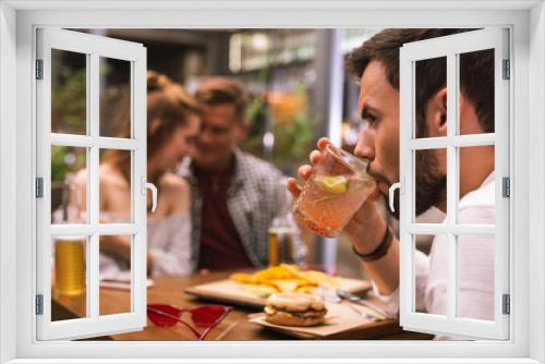 Cold drink. Serious young man drinking his cold cocktail while two of his friends flirting