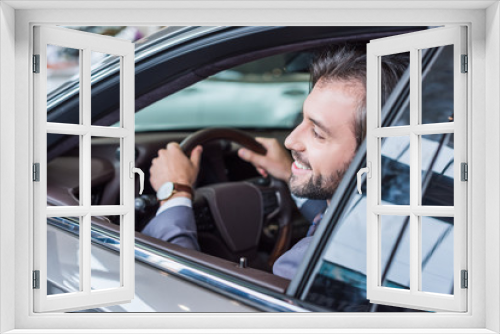 smiling businessman sitting in new car for test drive in dealership salon