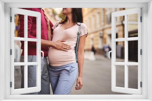 Tender moment. Cropped portrait of young bearded man hugging his beautiful pregnant wife and touching her belly. Smiling lady placing hand on husband chest