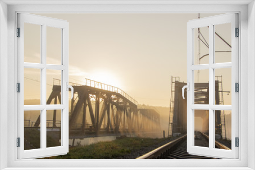 Fototapeta Naklejka Na Ścianę Okno 3D - A railway bridge in the morning fog or smoke through which the rays of the sun shine