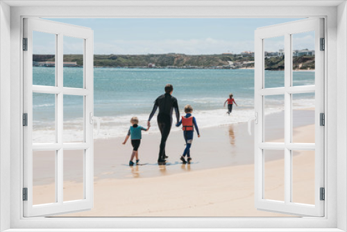Fototapeta Naklejka Na Ścianę Okno 3D - A young surfer walks with his children along the beach. Joint pastime. A happy family.