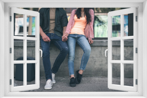 Couple on parapet. Young people wearing casual clothes and holding hands while sitting on the parapet