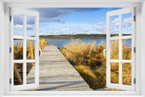 Fototapeta Naklejka Na Ścianę Okno 3D - Wooden jetty with railings on the lake named Gurino in Siberia with a cloudy blue sky and golden reed
