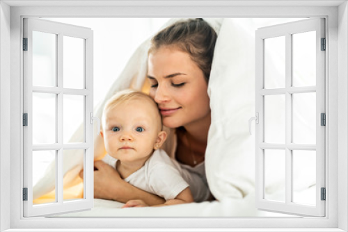 Portrait of young mother with infant baby girl liying on the bed covered with a white blanket