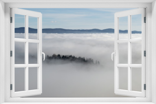 Fototapeta Naklejka Na Ścianę Okno 3D - A view from an high tower in the little town of San Gimignano, tuscany italy. A sea made of fog until the horizon with light blue mountains in the background and a little town emerging from the mist 