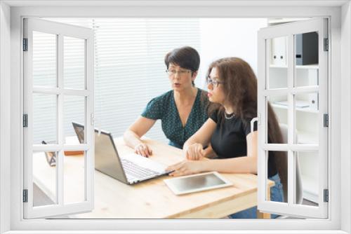 Office, business people and graphic designer concept - Women sitting and discussing ideas at the office with laptop, looking at the screen, listening to opinions