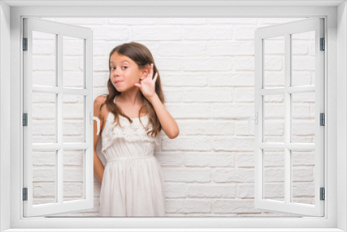 Young hispanic kid over white brick wall smiling with hand over ear listening an hearing to rumor or gossip. Deafness concept.