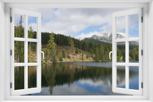 Fototapeta Naklejka Na Ścianę Okno 3D - Strbske pleso and Tatra peaks visible from the back. A village located in the valley, from which tourists are moving to the Tatras. Colorful waters of a mountain pond, blue sky and unending peaks.