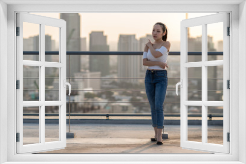 Portrait of Asian Yong woman in sexy fashion suit standing on the rooftop over the cityscape background, beautiful shape of body concept