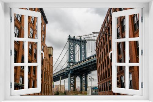 Fototapeta Naklejka Na Ścianę Okno 3D - Manhattan Bridge Viewed From Dumbo, Brooklyn, New York between two red brick buildings and cloudy background