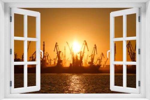 Fototapeta Naklejka Na Ścianę Okno 3D - Many big cranes silhouette in the port at golden light of sunrise reflected in water. Berdiansk, Ukraine