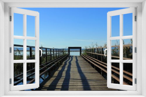 Fototapeta Naklejka Na Ścianę Okno 3D - Wooden boardwalk and bridge connecting two shores over a canal gate at the end view of the sea and mountains  at the background at koronisia village in Greece