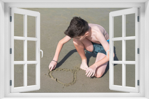 Fototapeta Naklejka Na Ścianę Okno 3D - Boy in the swimming trunks draws shape of heart on the sand on the beach .  Concept