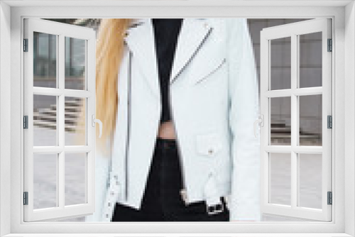 Blonde woman in the urban background. Beautiful young girl wearing a white leather jacket standing in the street.