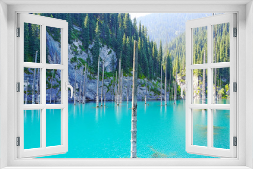 Fototapeta Naklejka Na Ścianę Okno 3D - Coniferous tree trunks rise from the depths of a mountain lake with blue water. Shooting with the drone. At the edges of the lake green forest and coniferous trees. Kazakhstan, Almaty, Kaindy lake.
