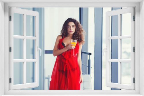 Curly woman drinking juice in red dress